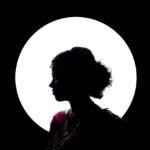 Artistic silhouette of a bride in traditional attire against a dramatic circular light.