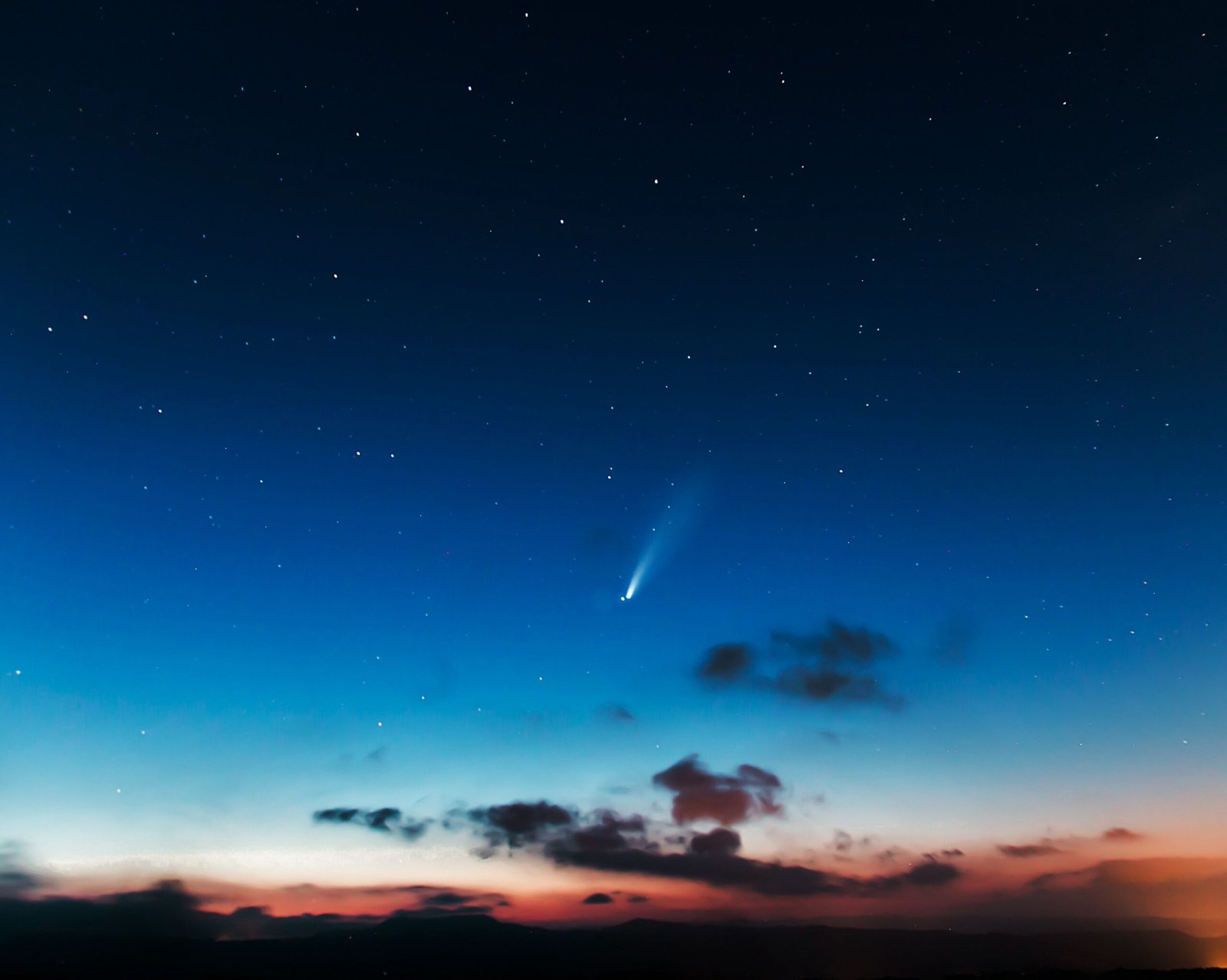 Spectacular view of a night sky with a bright comet and numerous stars above the horizon.